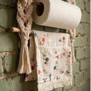 Handmade macrame kitchen organizer and coffee corner wall hanging holding porcelain cups, a paper towel roll, and a hand towel by Kemet Vibes.