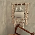 Handmade macrame kitchen organizer and coffee corner wall hanging holding porcelain cups, a paper towel roll, and a hand towel by Kemet Vibes.