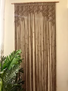 Handmade earthy leaf macrame curtain and large wall hanging by Kemet Vibes hung on a wooden dowel in a sunlit room