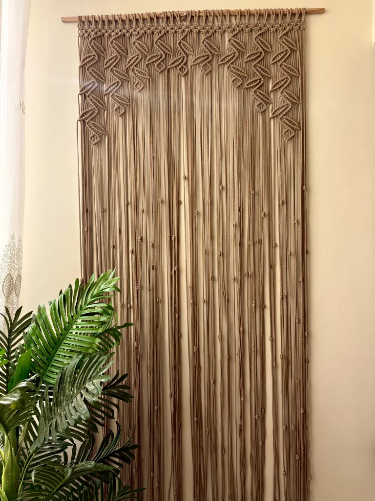 Handmade earthy leaf macrame curtain and large wall hanging by Kemet Vibes hung on a wooden dowel in a sunlit room